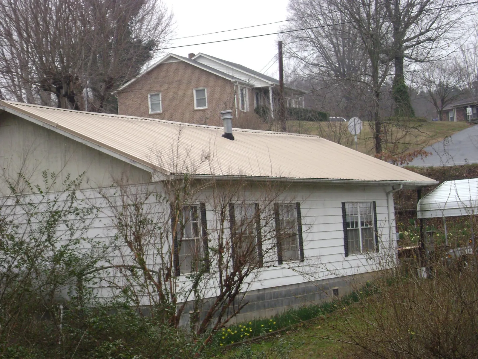 Tan metal roof on a white sided house set into a hillside — Commercial Roofing by Roofing Brothers in Elizabeth